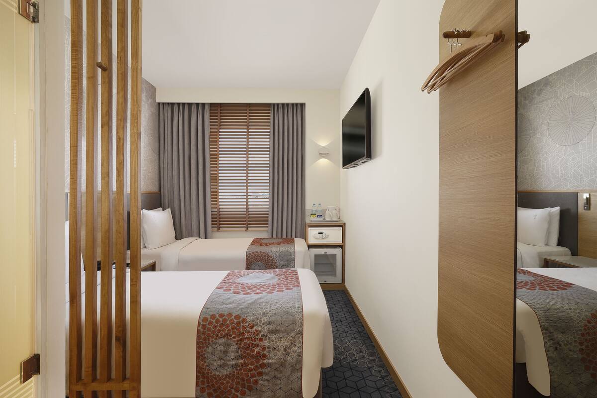 A hotel room with two beds, a desk, a TV, and a mirror.