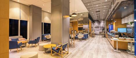 A modern hotel lobby with seating areas, a reception desk, and a staircase leading to an upper level.