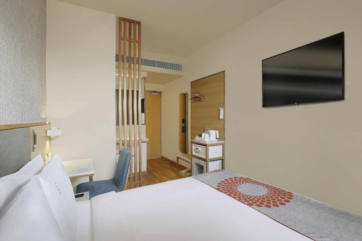 A hotel room with a bed, a desk, a chair, a TV, a mirror, and a wardrobe.