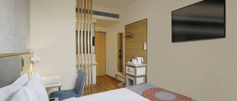 A hotel room with a bed, a desk, a chair, a TV, and a bathroom with a mirror and towel rack.