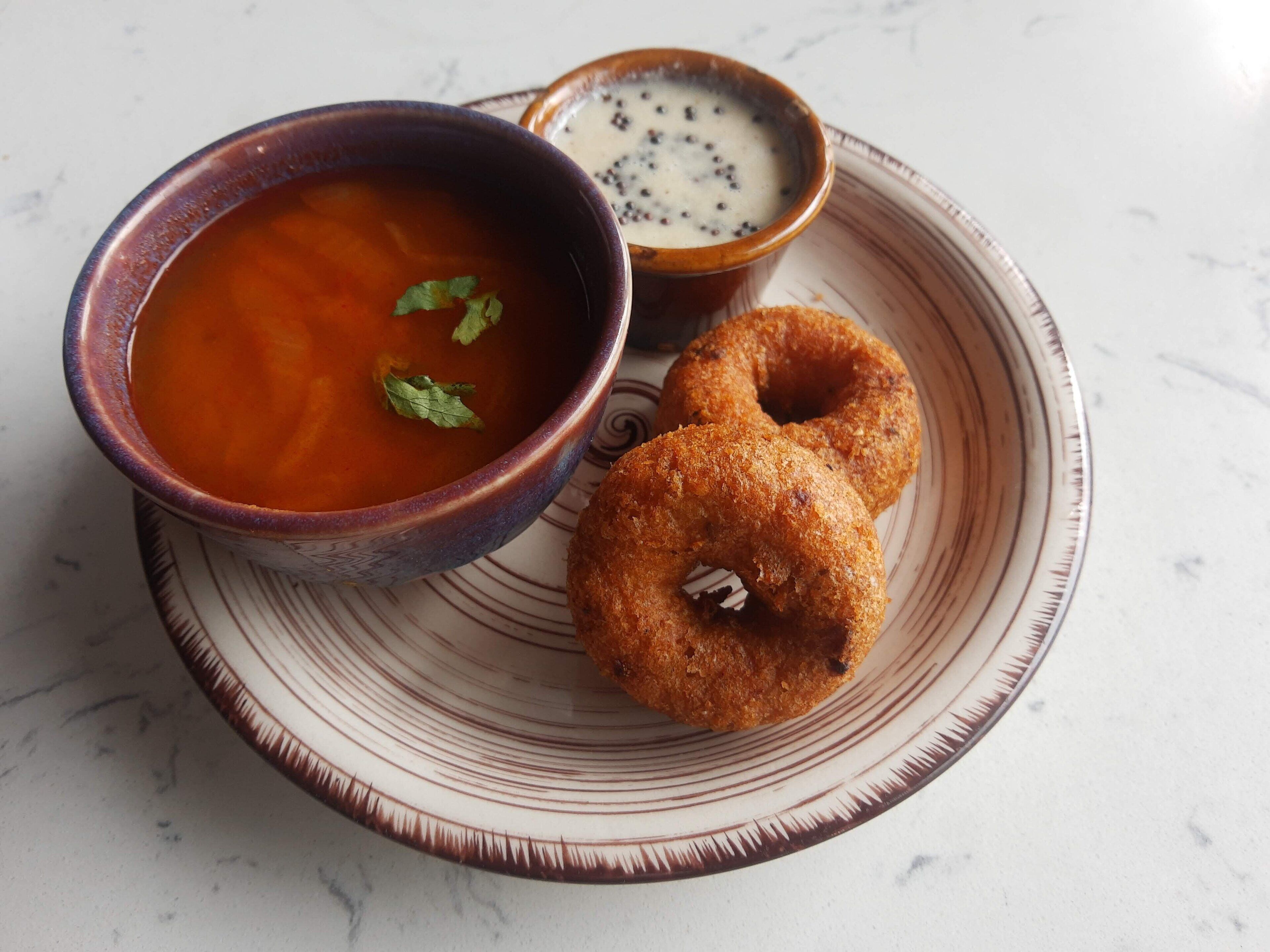 Un plato con un tazón de sopa, un tazón pequeño de salsa y dos buñuelos fritos.