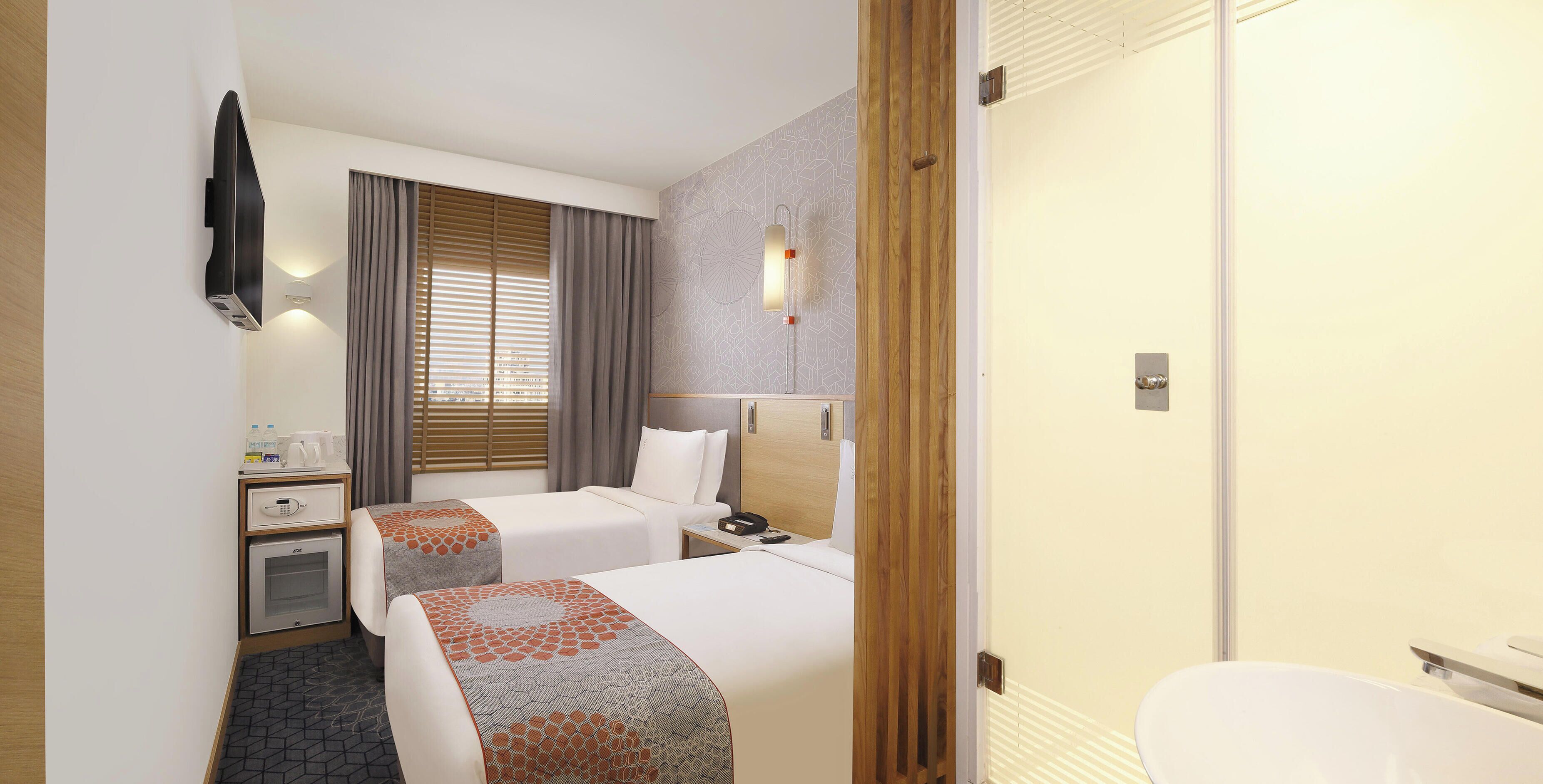 Une chambre d’hôtel avec deux lits, un bureau avec un téléphone, un petit placard et une salle de bain avec des toilettes et un lavabo.