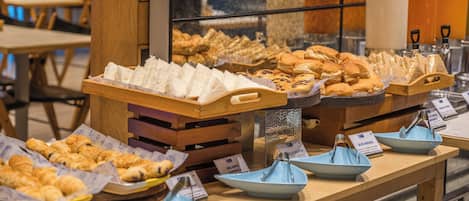 Un buffet de petit-déjeuner proposant diverses viennoiseries et pains présentés sur des présentoirs en bois.