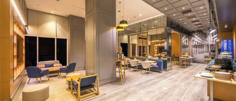 Un moderno vestíbulo de hotel con zonas de estar, un mostrador de recepción y un comedor.