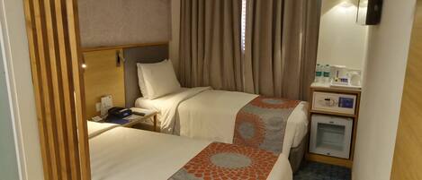 A hotel room with two beds, a bedside table with a phone, a small desk with a computer, a microwave, and a mini-fridge.