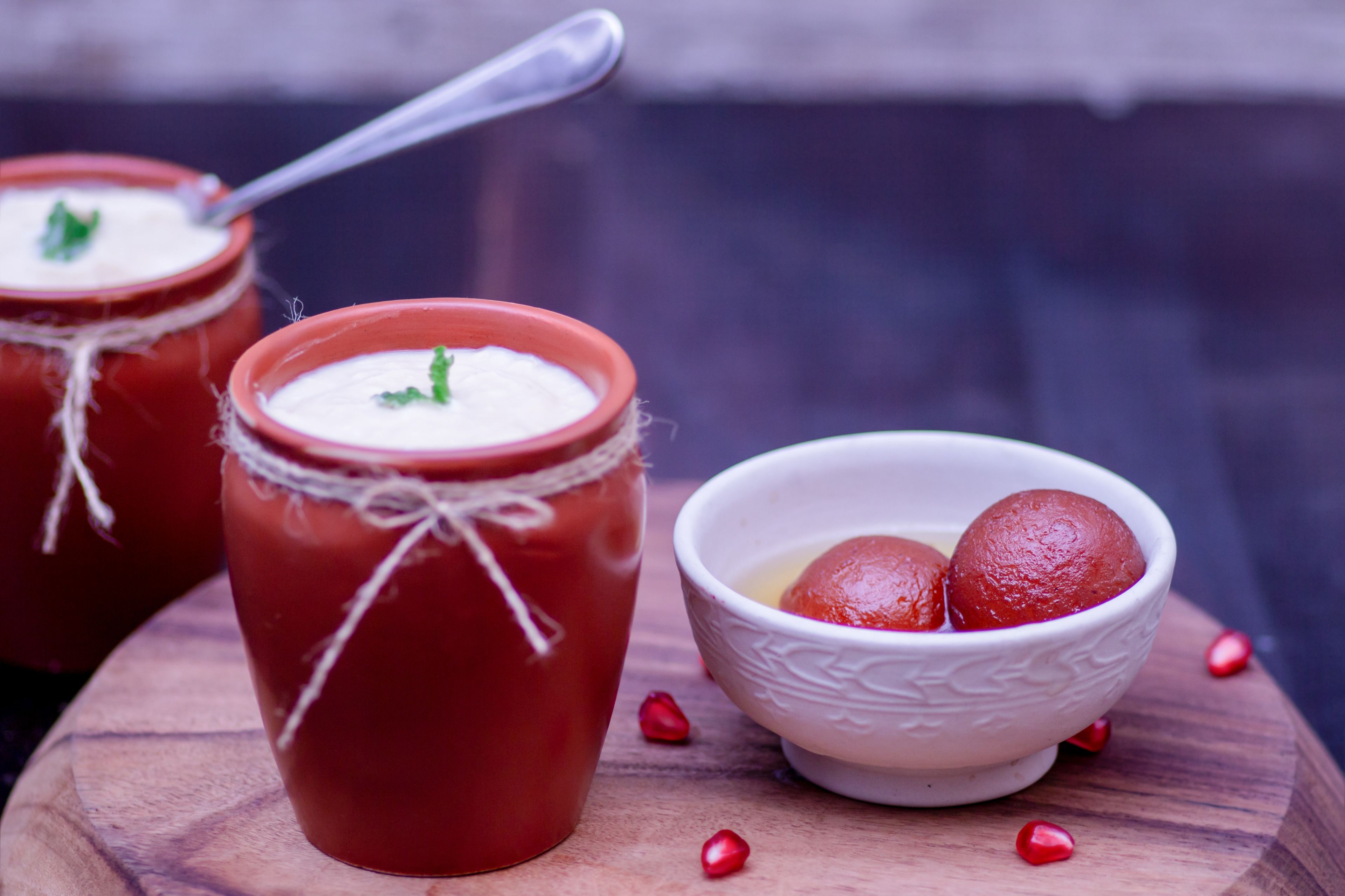Two red ceramic cups with white cream and mint garnish, and a white bowl with red sweets on a wooden surface.