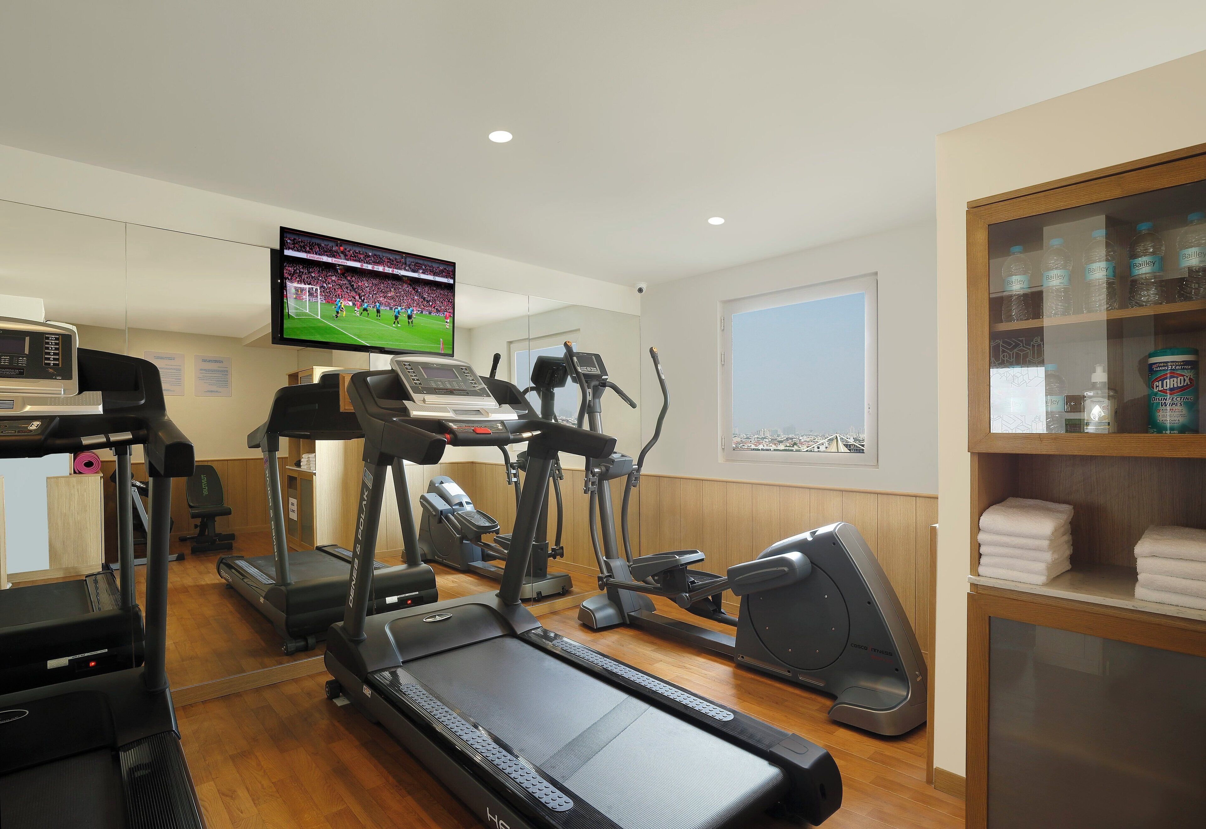 Gimnasio con cintas de correr, bicicleta estática y una televisión mostrando un evento deportivo.