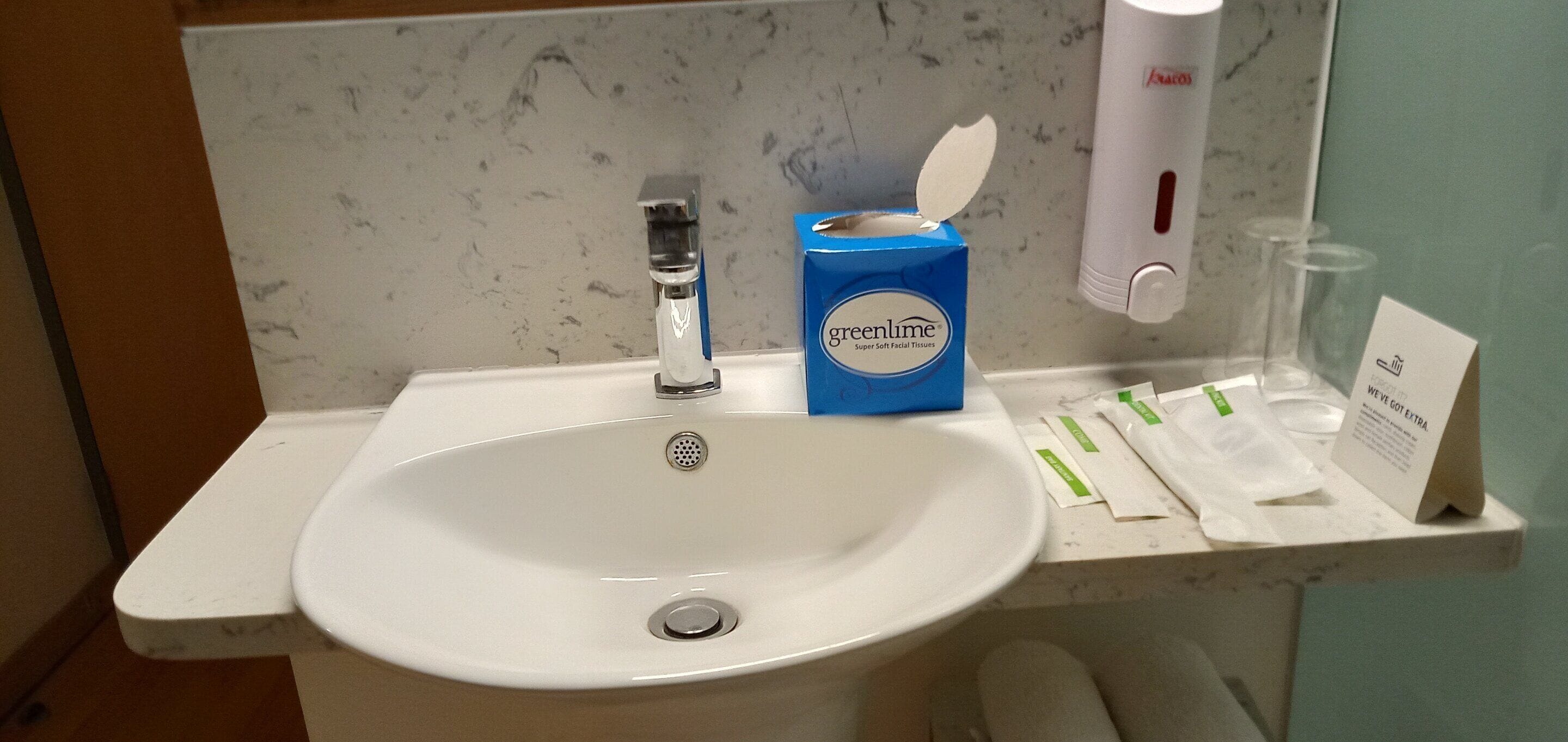 A bathroom sink with a blue tissue box labeled 'Greenlime' and a hand soap dispenser.