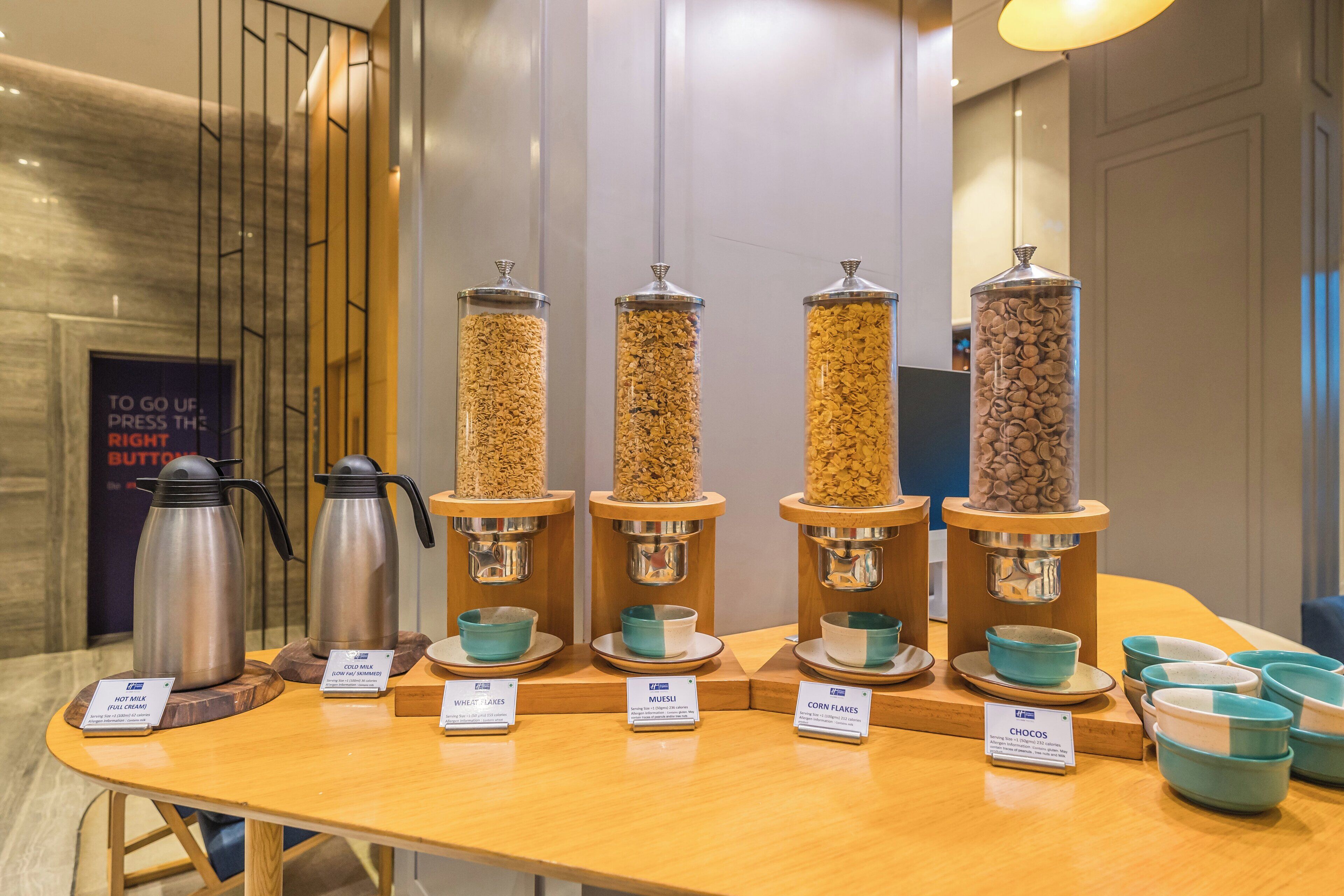 Una estación de café con dispensadores para leche caliente, leche fría, copos de trigo, muesli, copos de maíz y chocos.