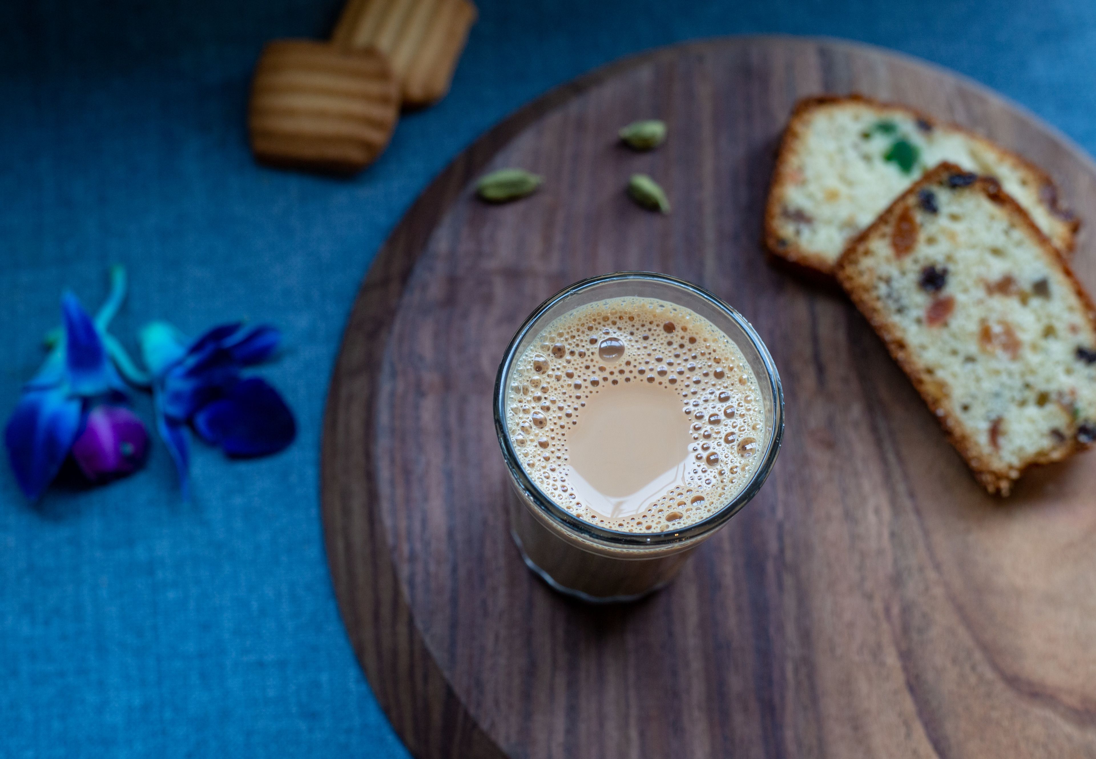 A glass of coffee on a wooden board with slices of bread and a flower.
