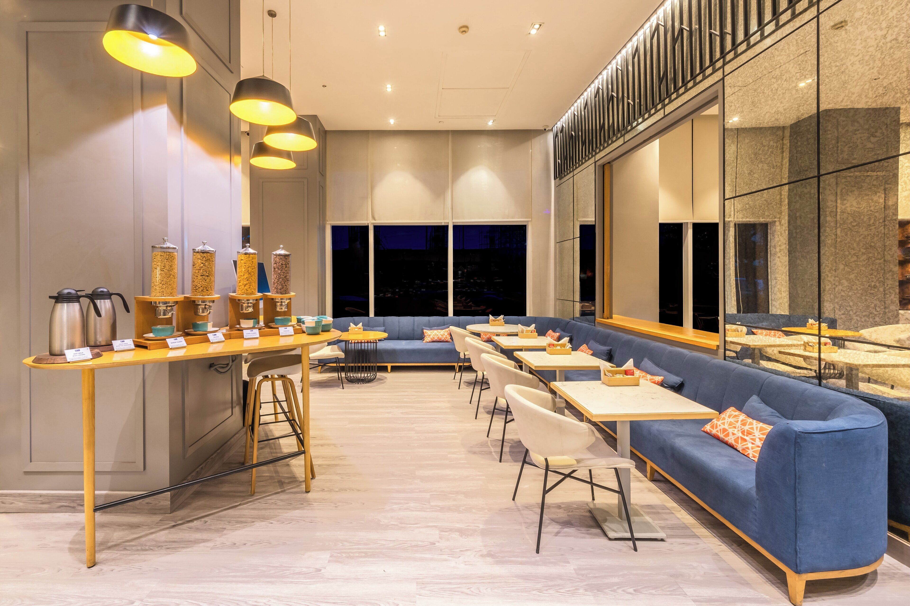 A modern restaurant with a long counter, blue seating, and pendant lighting.