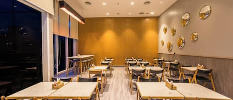 Un restaurante con varias mesas y sillas, piso de madera y una pared con espejos circulares.