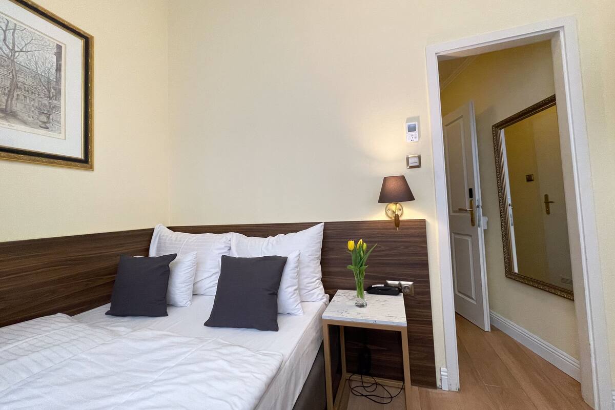 Una habitación de hotel con cama, mesita de noche, lámpara y un cuadro en la pared.