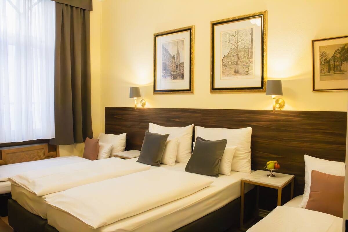 Habitación de hotel con dos camas, cabecera de madera, obras de arte enmarcadas en la pared y una mesita de noche con lámpara.