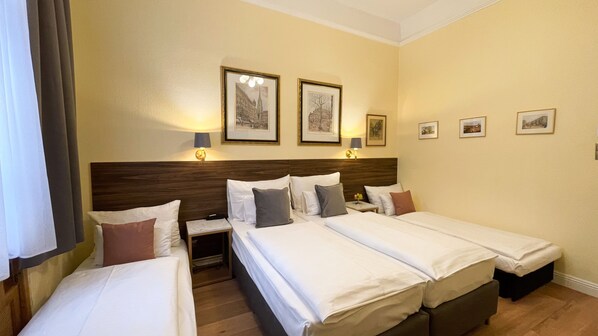 Camera d'albergo con due letti, un comodino e una parete decorata con quadri.