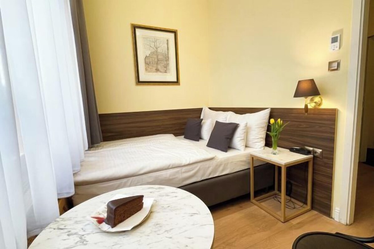 A hotel room with a bed, a bedside table with a vase of flowers, a lamp, and a framed picture on the wall.
