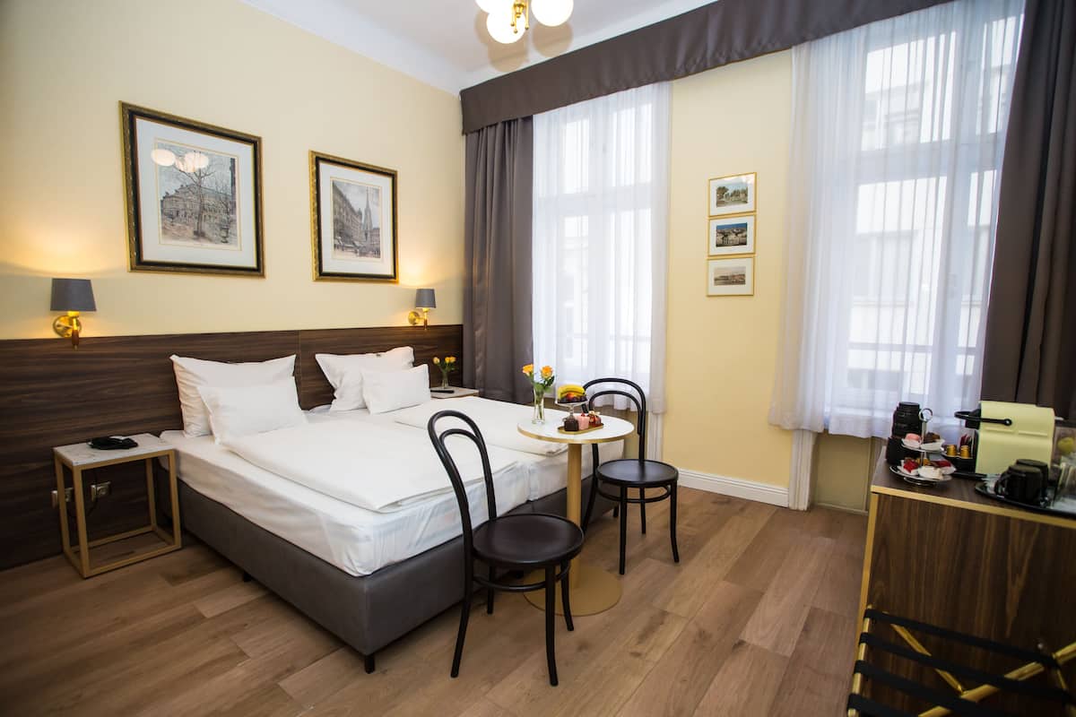 Habitación de hotel con cama, dos sillas, una mesita, una mesita de noche y un escritorio con lámpara.