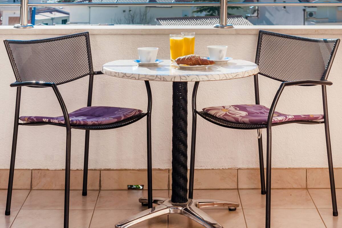 Ein Balkon mit Tisch und zwei Stühlen, mit Blick auf die Küste.