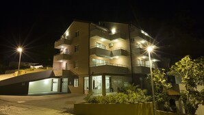 A multi-story building with balconies, a ground-level entrance, and a parking area. - Apartments Vila Adrijana and Fitness Studio Wolf (Baska Voda)