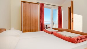 A hotel room with a bed, a wooden wardrobe, and a balcony with red curtains. - Apartments Vila Adrijana and Fitness Studio Wolf (Baska Voda)