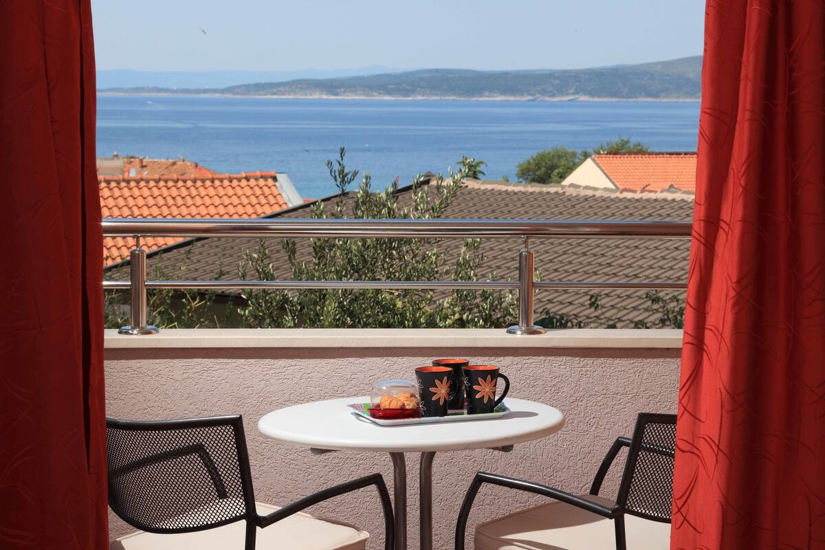 Ein Balkon mit Tisch und Stühlen, Blick aufs Meer und roten Vorhängen.