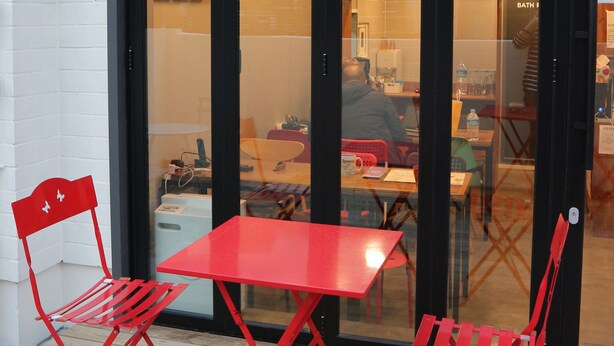 A red table and two red chairs outside a building with a glass door. - Zzzip Guest House - Hostel (Seoul)