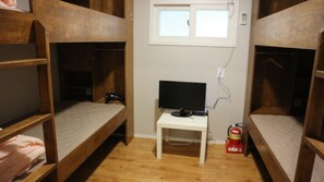 A dormitory room with bunk beds, a small white table with a television, and a window above.