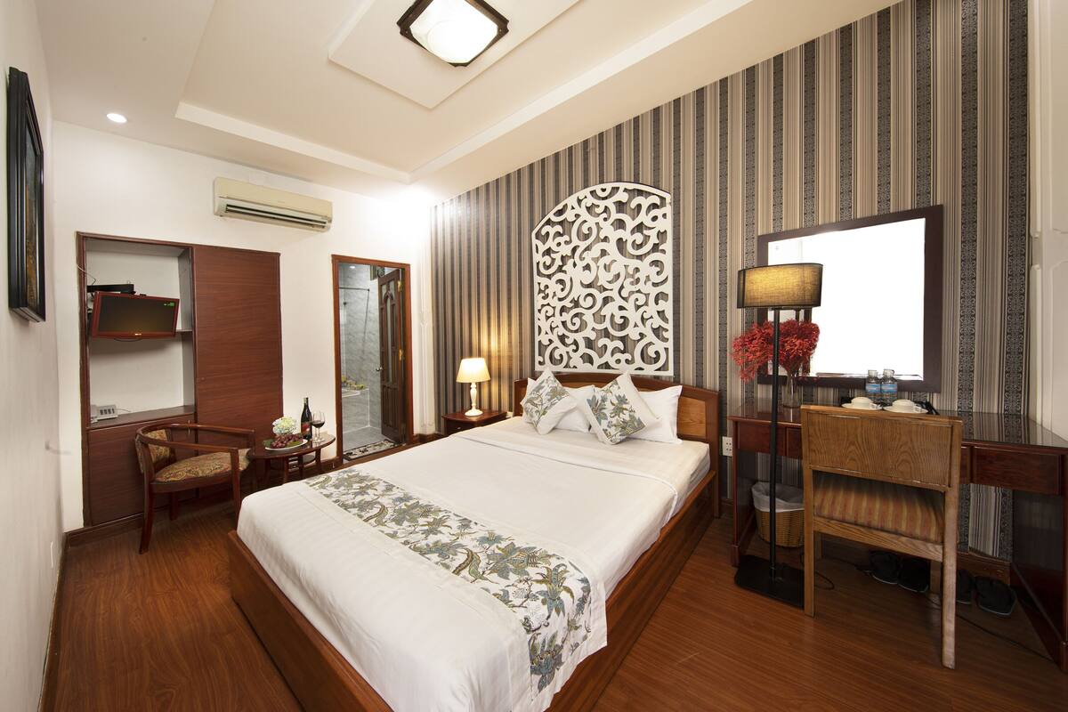 A hotel room with a large bed, a desk, a chair, a mirror, and a decorative wall panel.