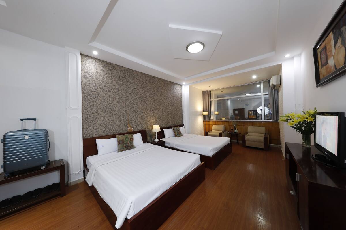 A hotel room with two beds, a small desk, a chair, a TV, and a suitcase.