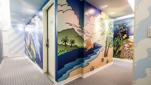 A hallway with a mural depicting a beach scene, including palm trees, a whale, and a diver. - Morwing Hotel - Ocean (New Taipei City)