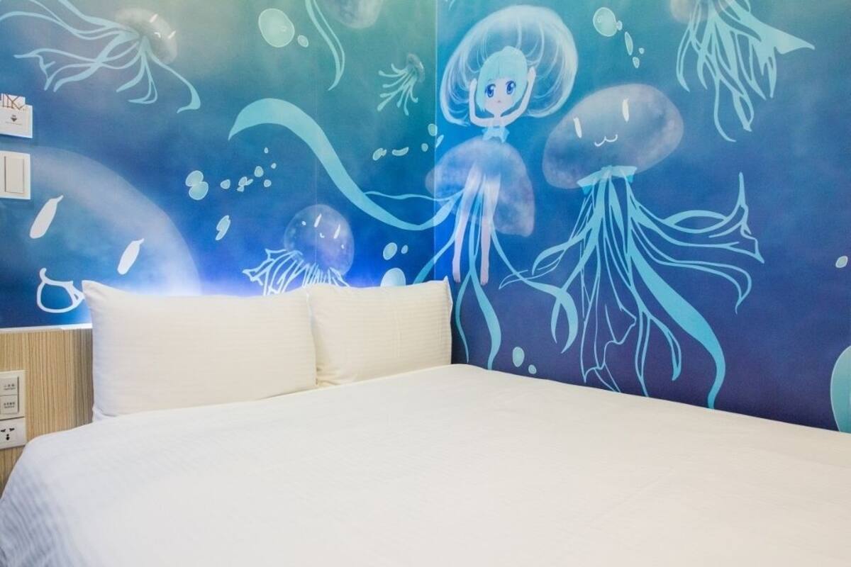 A hotel room with a bed, a wall with an underwater-themed mural, and a night switch on the wall.