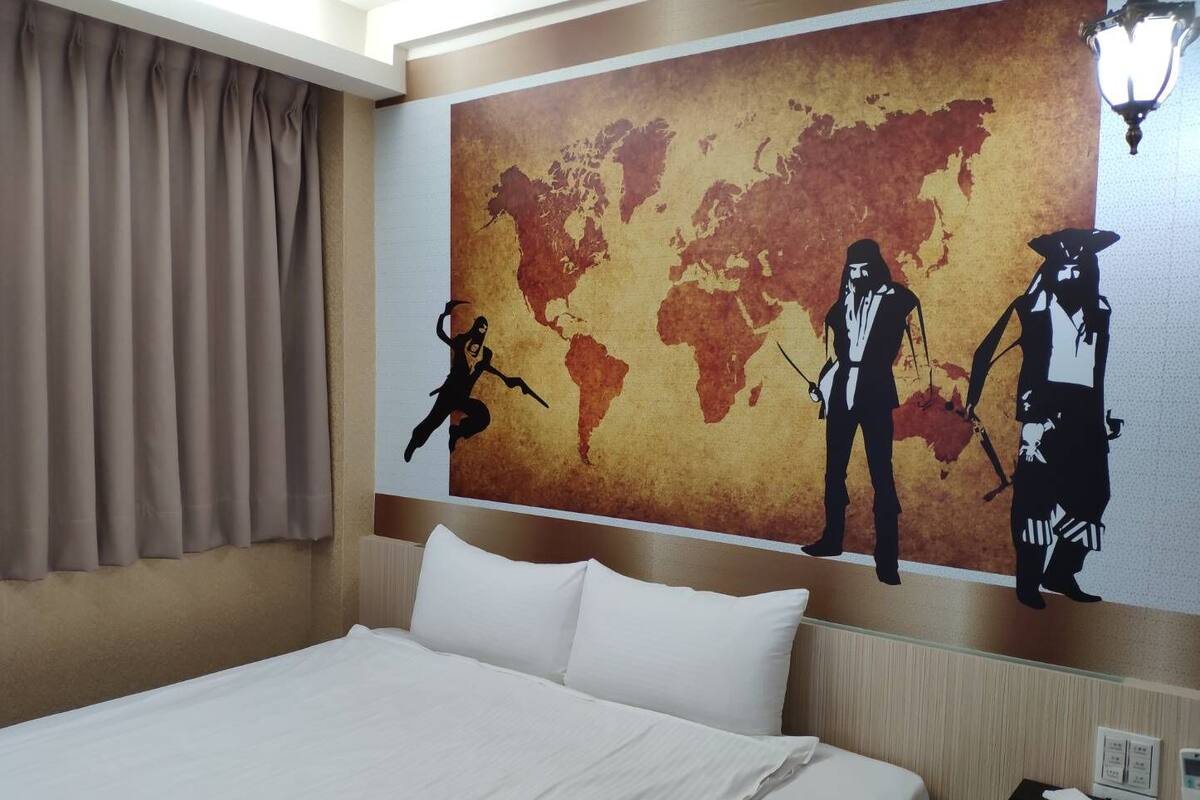 A hotel room with a large bed, beige curtains, and a world map mural on the wall.