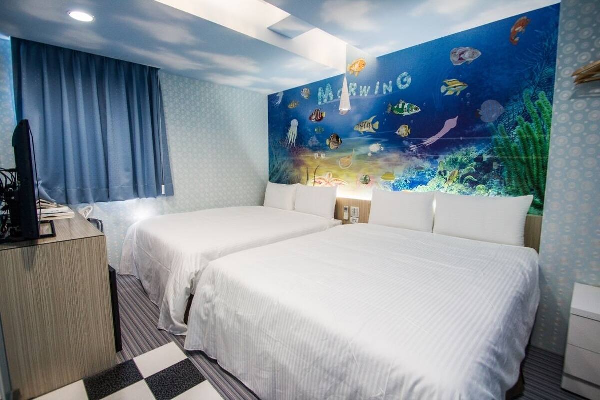 A hotel room with two beds, a desk, and a mural of an underwater scene on the wall.