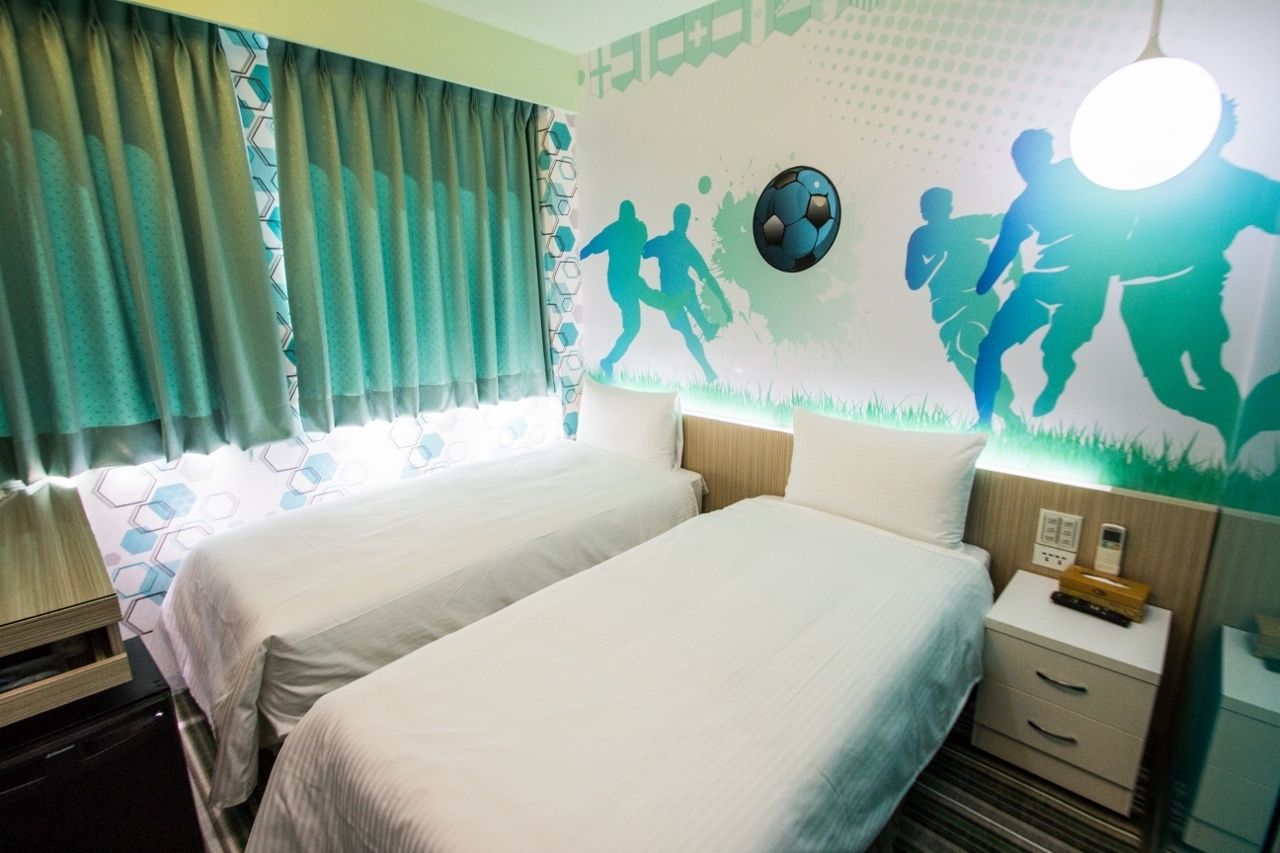 Une chambre d’hôtel avec deux lits, une table de chevet, une lampe et une fresque murale représentant des joueurs de football.