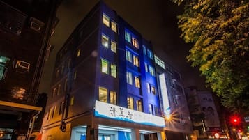A multi-story hotel with illuminated signage and windows, located on a city street at night.