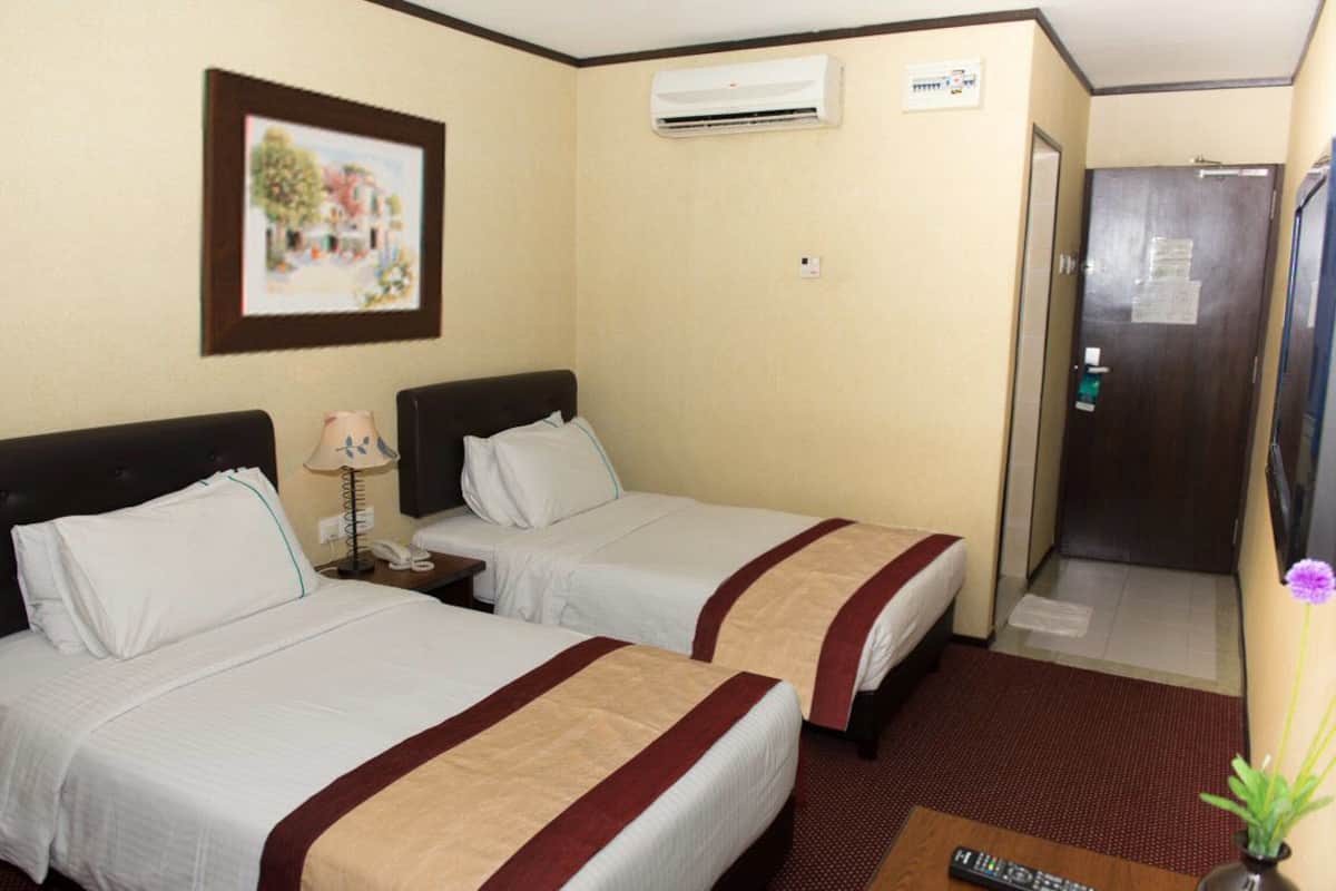 Camera d'albergo con due letti, un quadro appeso al muro, un condizionatore e una porta con un cartello.