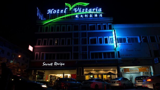 Hotel Vistaria with a neon sign, a visible storefront named 'Secret Recipe', and several parked cars in front. - Hotel Vistaria (Johor Bahru)