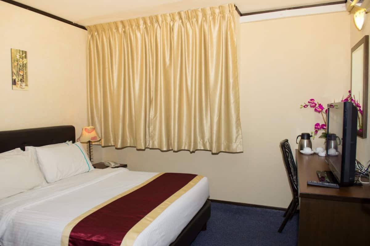 Una camera d'albergo con un letto, una scrivania con un computer, una sedia e una finestra con tende.