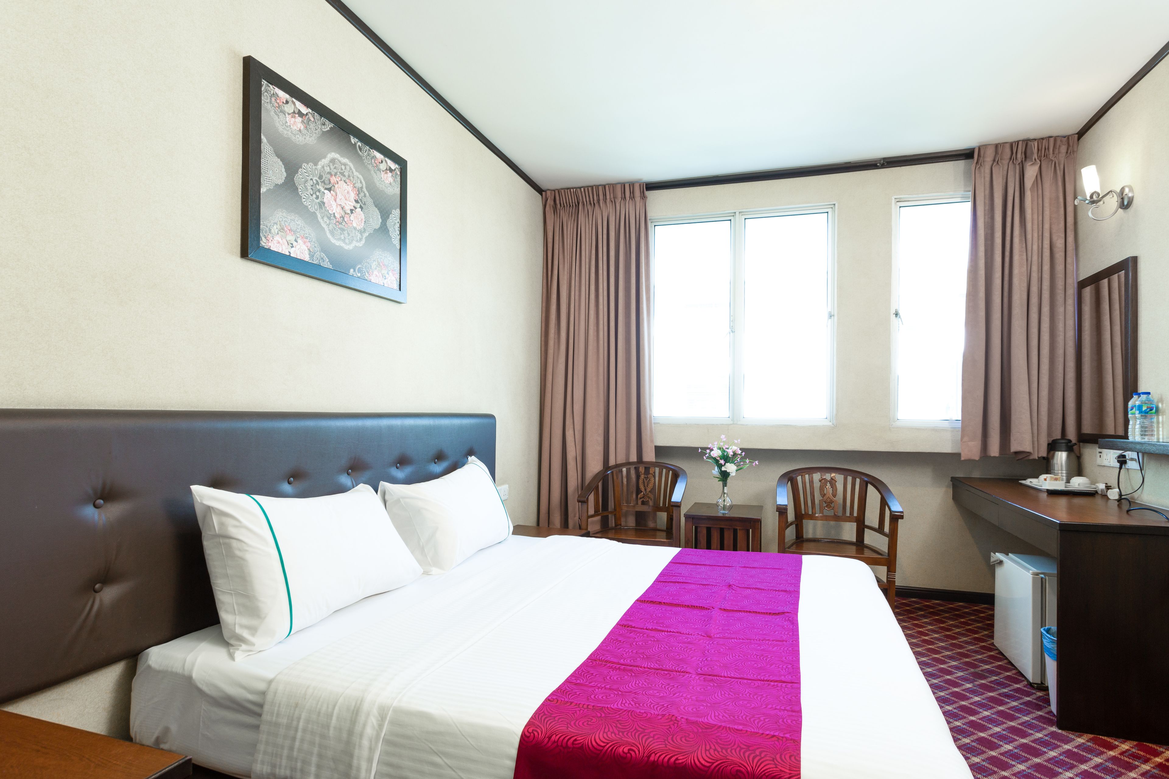 A hotel room with a large bed, a desk, a chair, and a window with curtains.