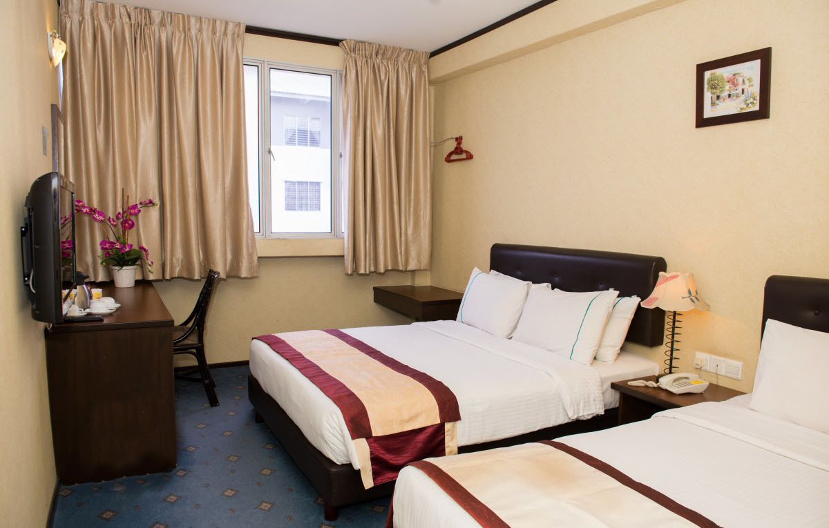 A hotel room with two beds, a desk with a lamp, a telephone, and a window with curtains.