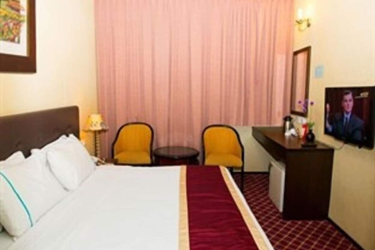 Una camera d'albergo con un letto, due sedie, una scrivania, un televisore e una tenda.