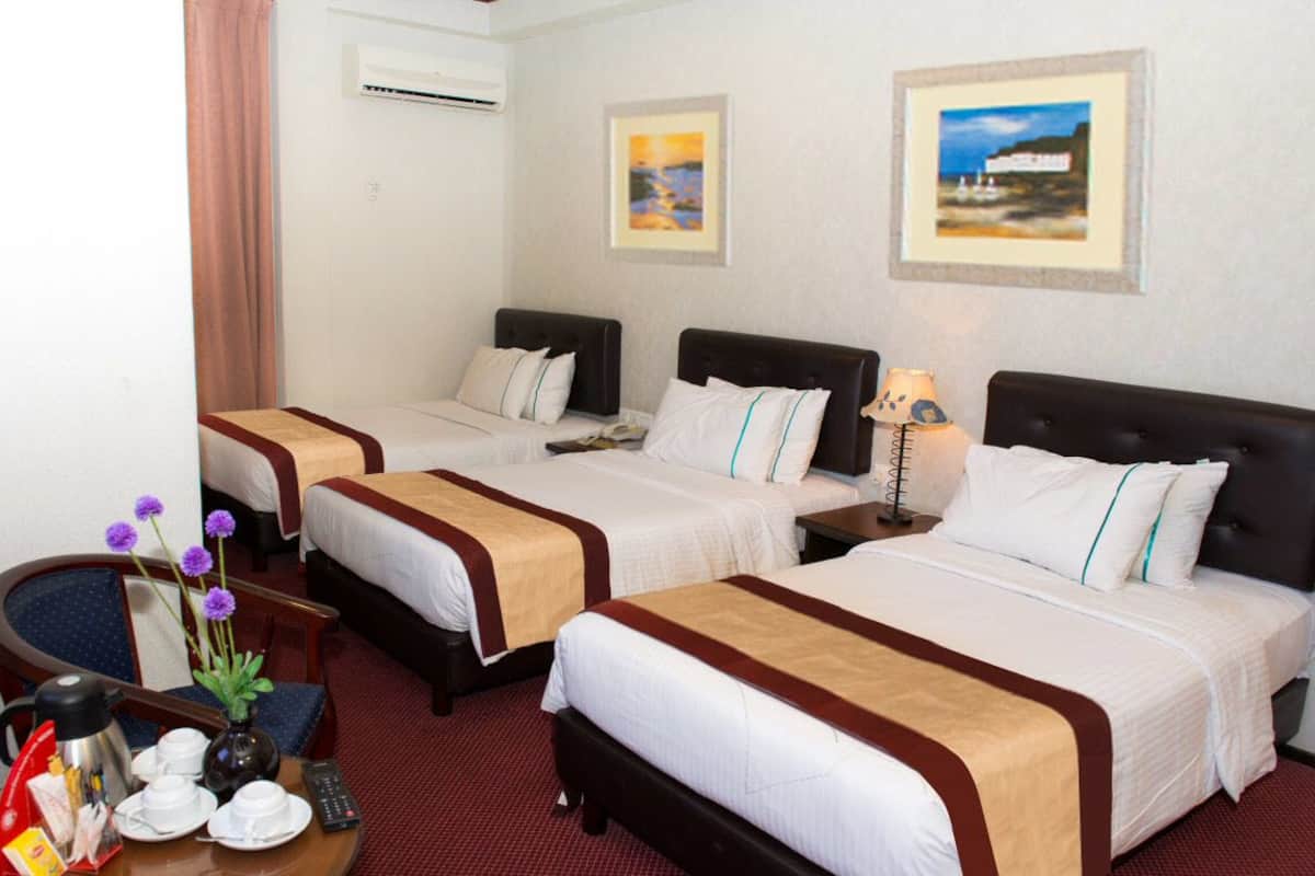 Camera d'albergo con due letti, una scrivania con lampada, una sedia e un piccolo tavolo con un vaso di fiori.