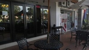 An outdoor seating area with metal tables and chairs, a glass storefront, and a sign above the entrance. - Hotel Vistaria (Johor Bahru)