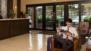 A reception area with a counter, chairs, and a person reading a magazine. - Hotel Vistaria (Johor Bahru)