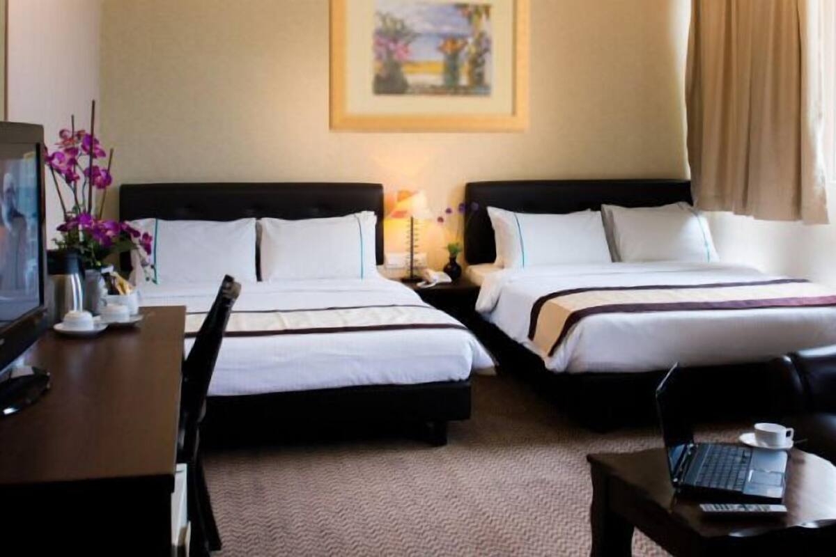 Una camera d'albergo con due letti, una televisione, una scrivania con un portatile e un tavolino.