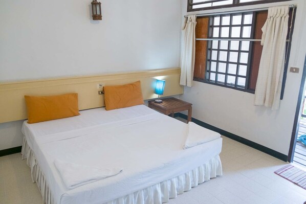 Habitación de hotel con una cama grande, una mesita de noche con lámpara, una ventana con cortinas y un aplique de pared.