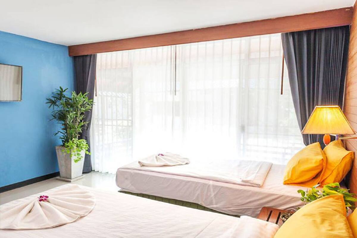 A hotel room with two beds, a potted plant, a lamp, and a window with curtains.