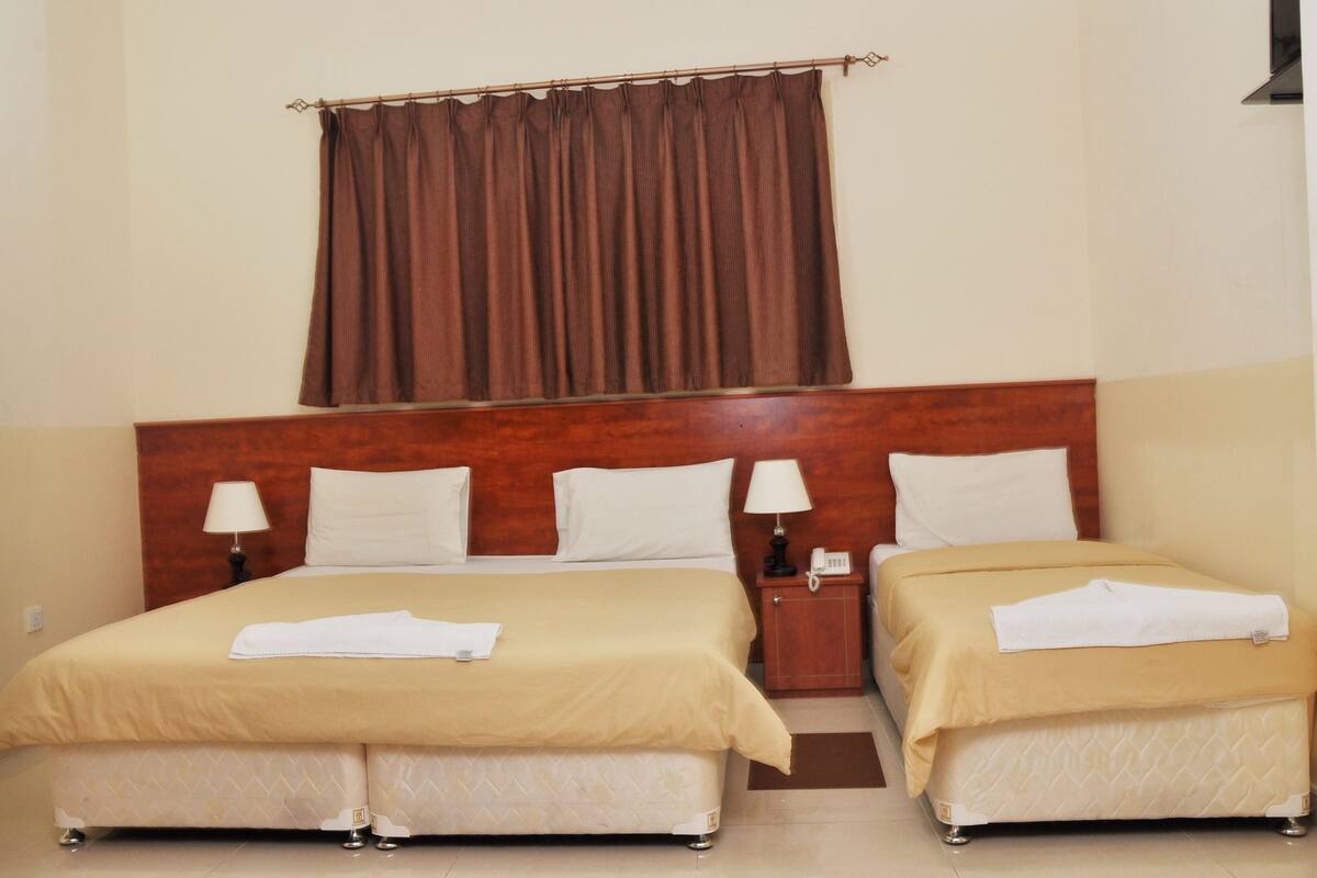 A double bed with a wooden headboard, two bedside tables with lamps, and a brown curtain.