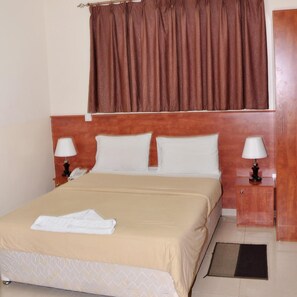 A hotel room with a bed, two bedside tables with lamps, a telephone, a brown curtain, and a wooden headboard. - Africana Hotel (Dubai)