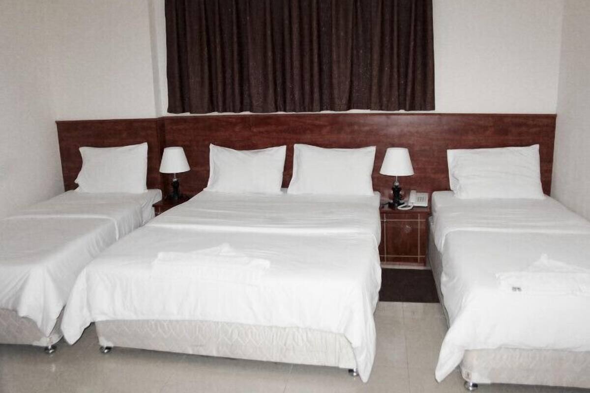 A hotel room with a large bed, two bedside tables, and a dark curtain.